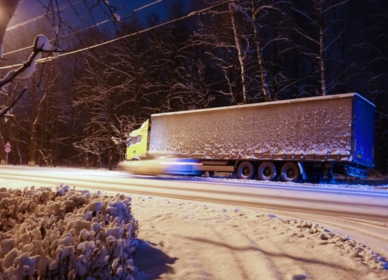 Truck with a cargo container on the side of a winter road. Silhouette of a passing car.