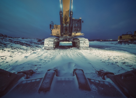 A large excavator on a snowy construction site at night. Long exposure with light painting.